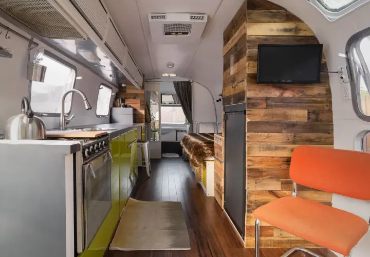 Intérieur d'une caravane Airstream rénovée, avec cuisine, lit douillet et mur en bois rustique.