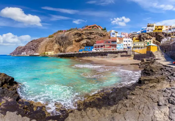 Plage de sable, maisons colorées accrochées à flanc de falaise, eaux turquoise. Idéal pour savoir que faire aux Canaries.