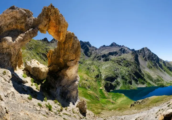Un arc rocheux spectaculaire domine un paysage de montagne verdoyant, avec des lacs bleus scintillants. Une vue digne d'une carte du Mercantour.
