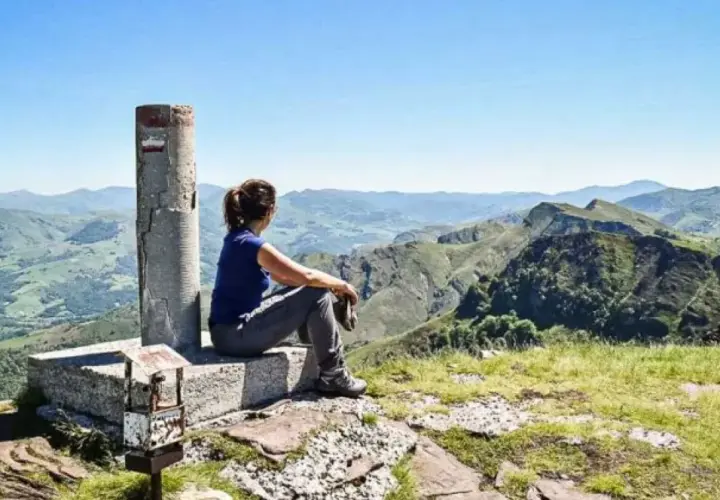 Vue panoramique sur les montagnes verdoyantes du gr pays basque. Une randonneuse contemple le paysage depuis un sommet.