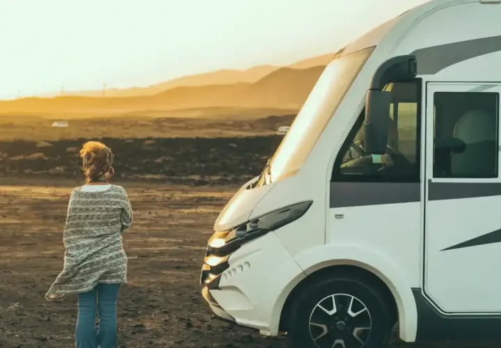 Une femme seule face à un camping-car dans un paysage désertique au coucher du soleil. Un lieu à éviter en camping-car pour son isolement.