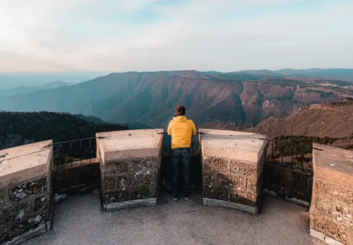 Un homme en jaune admire le panorama depuis le sommet du mont Aigoual, avec ses vastes étendues de montagnes bleues à perte de vue.