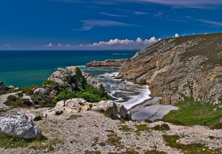Sentier rocailleux menant au **Cap de la Chèvre**, avec falaises abruptes plongeant dans une mer turquoise et un ciel bleu éclatant.