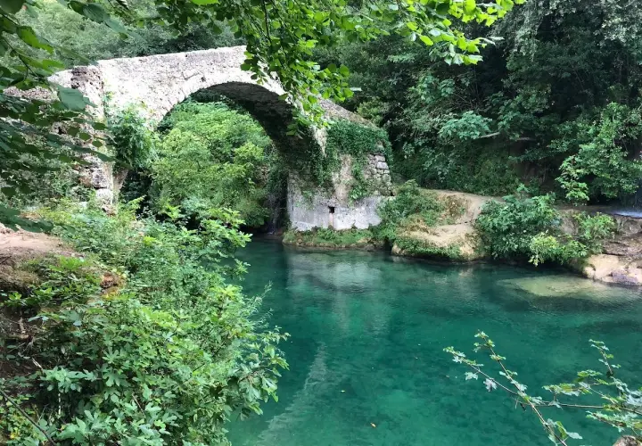 Un pont de pierre enjambe les eaux turquoise des gorges de la Siagne, entouré d'une végétation luxuriante.