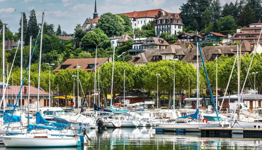 Port de plaisance à Thonon-les-Bains, avec des voiliers blancs et bleus amarrés, des maisons sur la colline et une église. Idéal pour savoir que faire à Thonon-les-Bains.