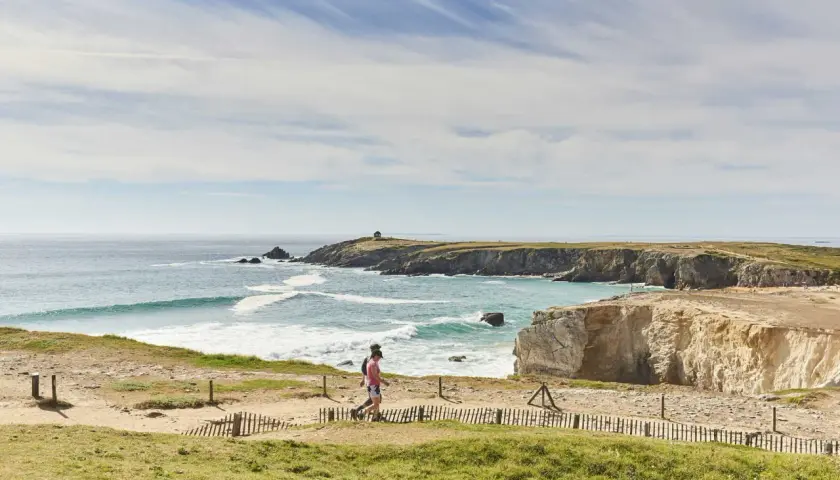 Deux randonneurs profitent du tour de la presqu'île de Quiberon à pied, longeant la côte rocheuse et la mer agitée sous un ciel bleu.