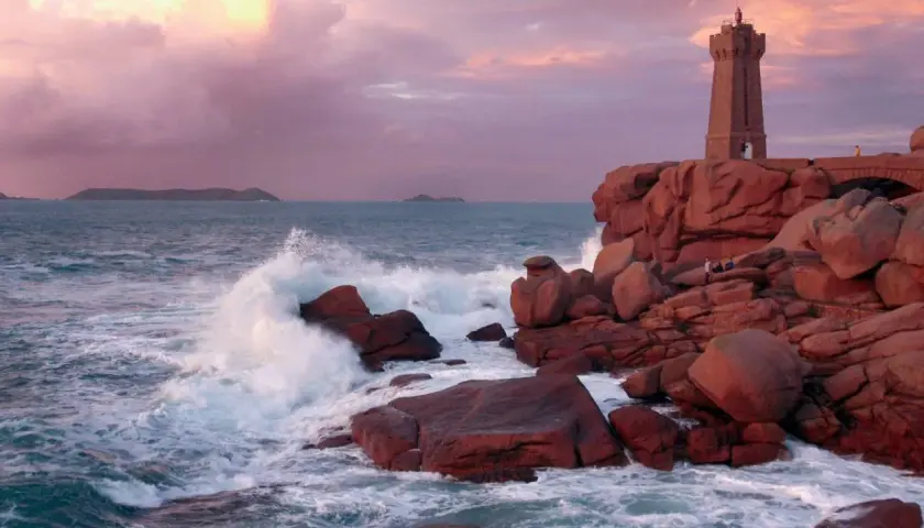Phare de Ploumanac'h, un joyau pour visiter la Bretagne. Vagues s'écrasant sur les rochers roses sous un ciel pastel.