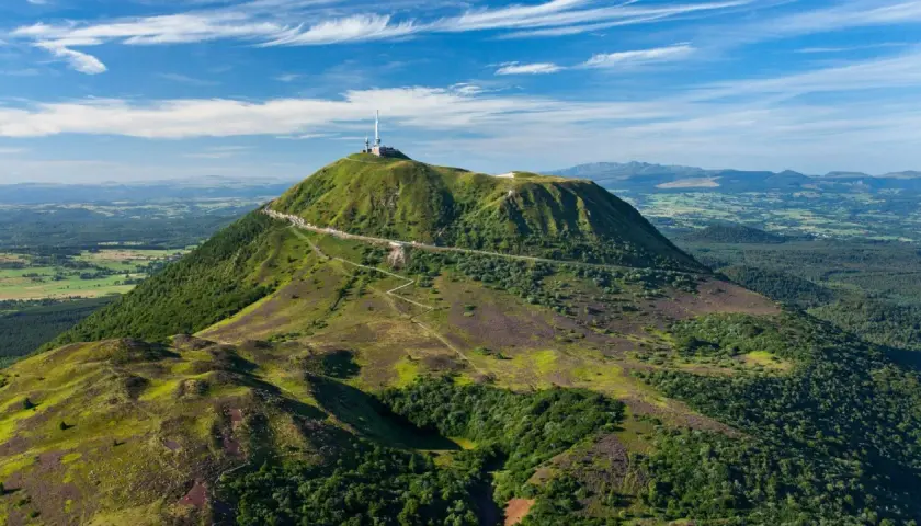 Vue aérienne du Puy de Dôme, un des volcans d'Auvergne, avec sa route en lacets et son antenne. Paysage verdoyant sous un ciel bleu.