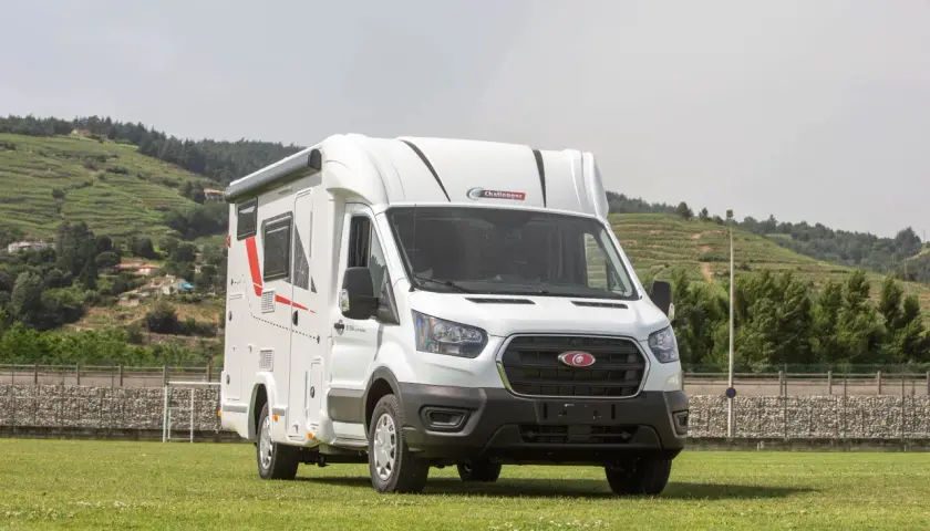 Porteur Ford camping-car blanc, prêt pour l'aventure sur un terrain verdoyant, avec des collines en arrière-plan.