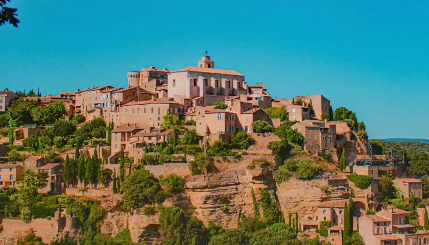 Village perché en Provence, idéal pour un budget vacances. Maisons en pierre, toits de tuiles, végétation luxuriante sous un ciel bleu.