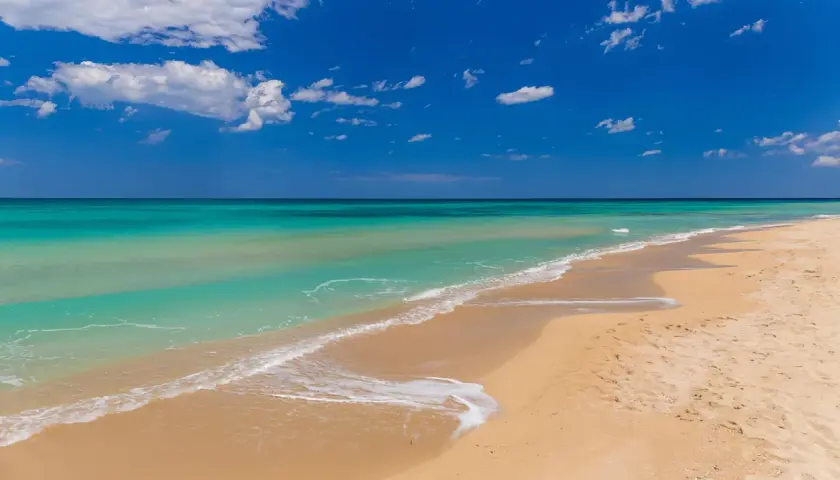 Plage de Bari, sable doré, eaux turquoise et ciel bleu azur avec des nuages blancs. Un rêve d'évasion.
