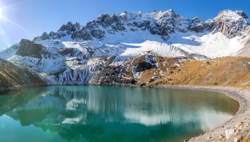 Lac d'altitude aux eaux turquoise, reflets des montagnes enneigées. Idéal pour une randonnée à Ceillac par temps ensoleillé.