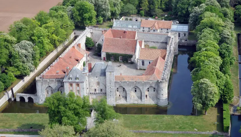 Vue aérienne du **château de Farcheville**, entouré de douves et de verdure. Ses toits de tuiles rouges contrastent avec les murs de pierre grise.
