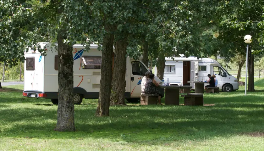 Des camping-cars stationnés dans un parc ombragé, des gens profitent de pique-niques. Un aperçu des plus belles aires de camping-car gratuites.
