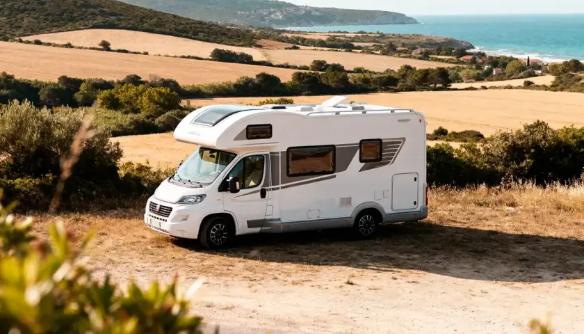 Camping-car blanc prêt pour une idée sortie week-end. Paysage de champs dorés et mer bleue en arrière-plan.