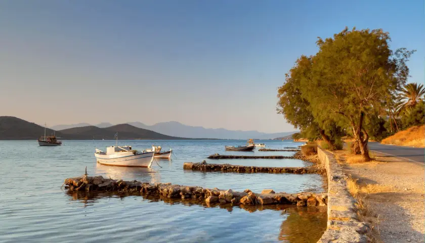 Bateaux blancs et bleus ancrés dans une baie paisible, avec des collines en arrière-plan, évoquant la sérénité de l'ile Crete.