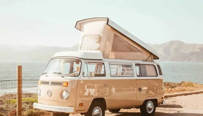 Un camping-car Volkswagen vintage, prêt pour l'aventure, avec son toit relevé, face à la mer et aux collines. L'esprit des 5 Terres en camping-car.