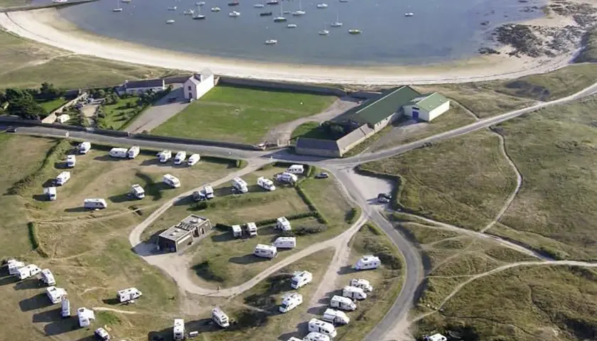 Vue aérienne d'une aire de camping-car finistère gratuit, avec des caravanes garées près d'une baie bordée de bateaux.