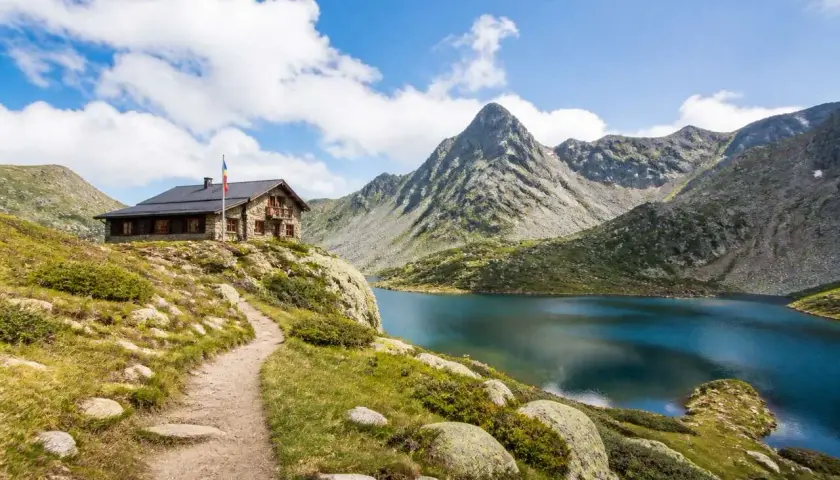 Sentier de randonnée en Andorre menant à un refuge de montagne près d'un lac alpin aux eaux bleues, avec des montagnes escarpées en arrière-plan.