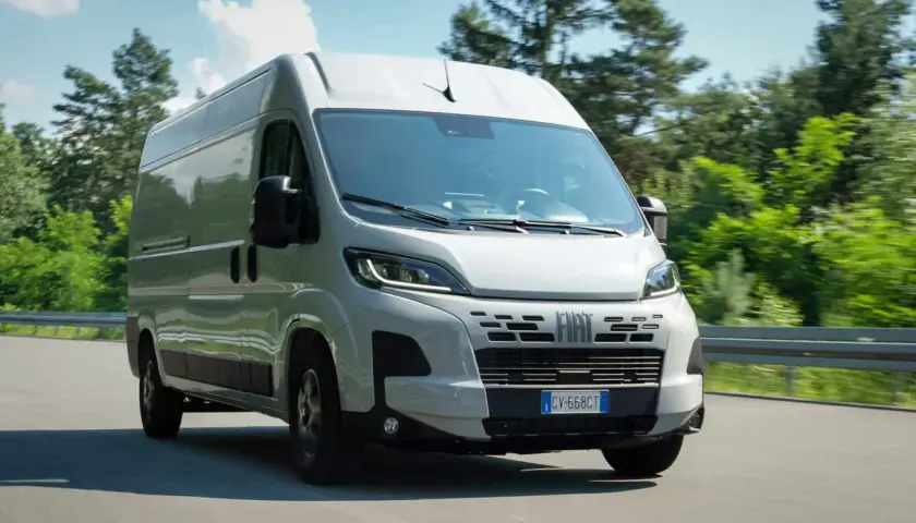 Un Fiat Ducato 2.2 Multijet 140 CV AdBlue blanc roule sur une route bordée d'arbres verts.