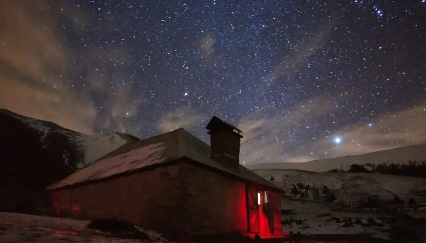 Un refuge illuminé par une lumière rouge sous un ciel étoilé. L'endroit parfait pour dormir en refuge après une longue journée.