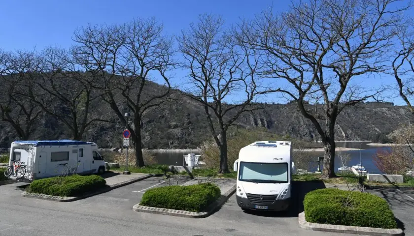 Stationnement pour camping-cars gratuit en Auvergne, avec vue sur le lac et les montagnes. Deux camping-cars sont garés sous des arbres dénudés.