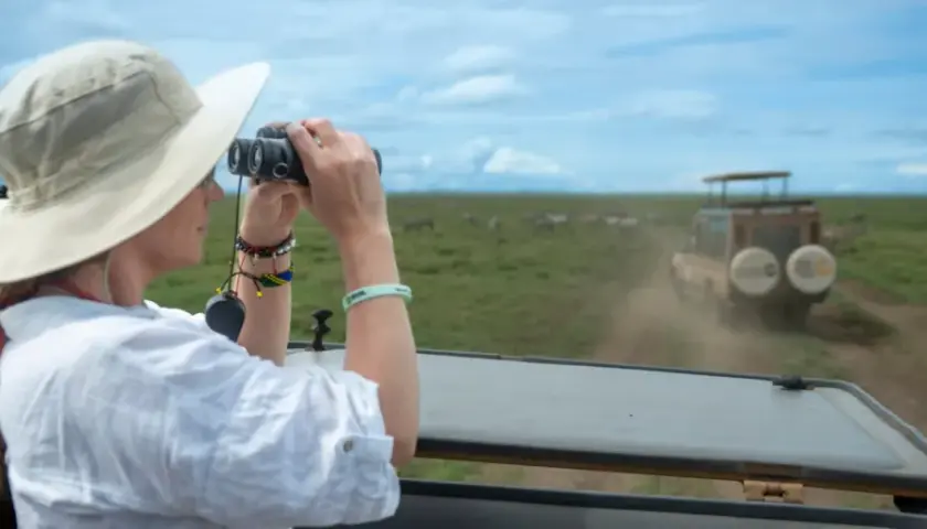Une femme en safari, jumelles à la main, observe des zèbres en Tanzanie. Une excellente idée de que faire en Tanzanie !