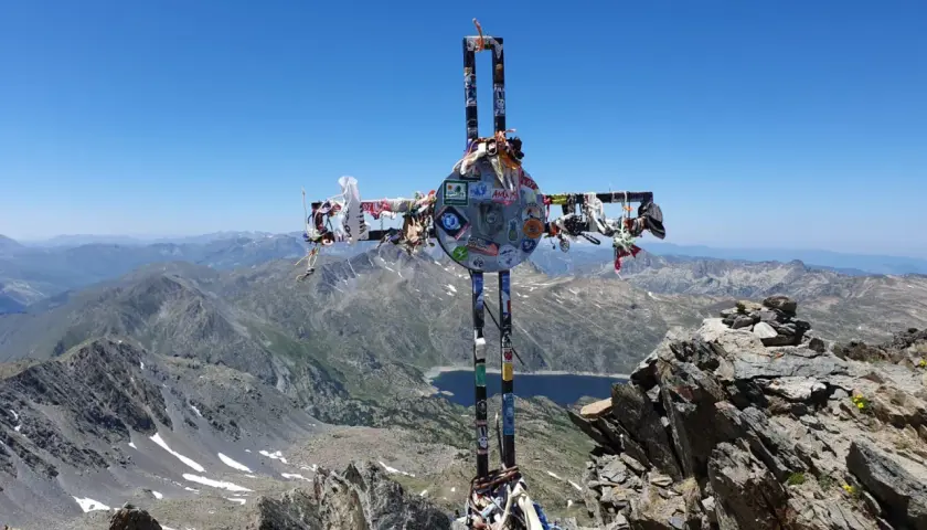 Croix ornée de souvenirs, au sommet d'une montagne, témoin d'un carlit randonnée mémorable. Paysage de haute altitude sous un ciel bleu.