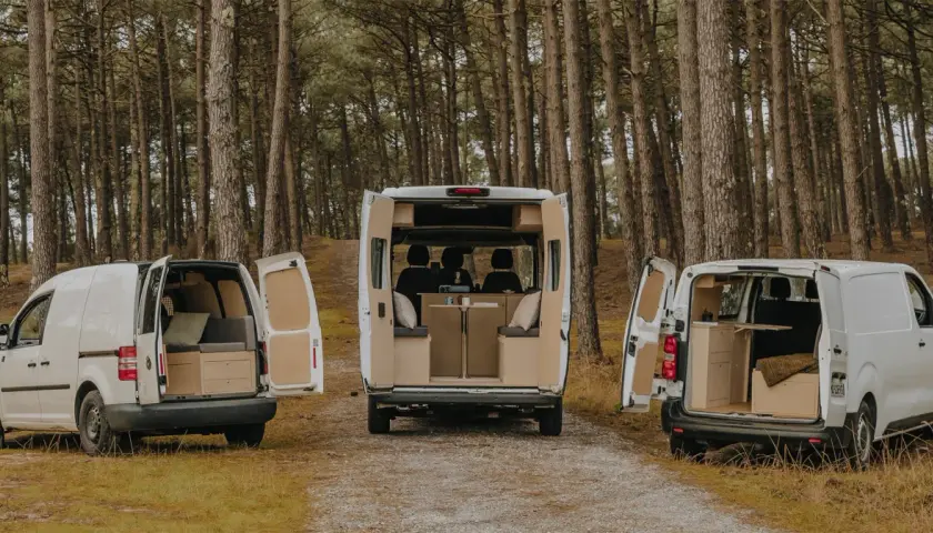 Trois camping-cars aménagés, dont un dimension camping-car 4 places, garés dans une forêt.