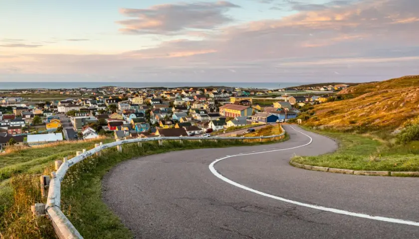 Vue panoramique de Saint-Pierre-et-Miquelon, avec ses maisons colorées nichées sur la côte et une route sinueuse menant au village.