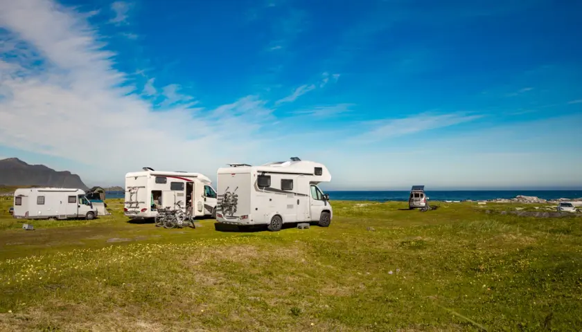 Plusieurs camping-cars stationnés sur une aire de camping car gratuite, face à la mer sous un ciel bleu.