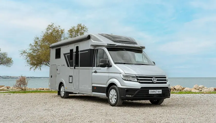 Camping car petite taille Adria Compact Max argenté, garé sur un chemin de gravier près de la mer.