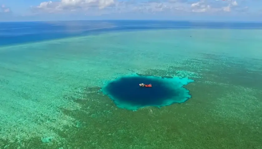 Un bateau rouge et blanc flotte au-dessus du trou du dragon, un abîme bleu profond entouré de récifs coralliens turquoise.