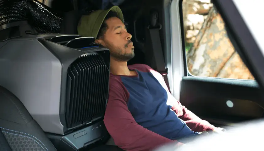 Un homme dort paisiblement dans son camping-car, grâce à un climatiseur portable. L'idéal pour une aire de camping-car gratuit avec électricité.
