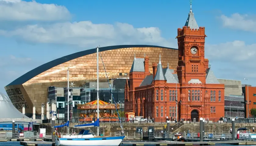 Bateaux amarrés dans le port de Cardiff, avec le bâtiment historique en brique rouge et le bâtiment moderne aux écailles cuivrées. Idéal pour visiter Cardiff.