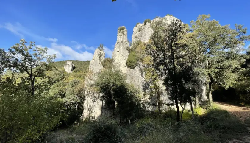 Les Aiguilles de Valbelle, formations rocheuses spectaculaires, se dressent sous un ciel bleu, entourées de verdure.
