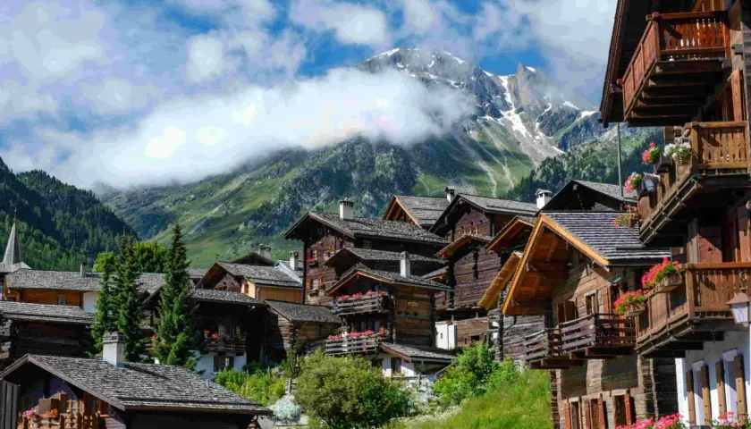 Villages de chalets en bois fleuris, montagnes enneigées en arrière-plan. Une belle idée de que faire en Suisse pour un séjour pittoresque.