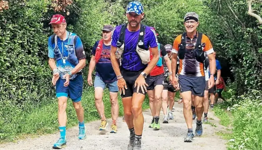 Coureurs en tenue de trail, certains avec des sacs d'hydratation, sur un sentier boisé. Le coureur au centre, portant une casquette bleue, semble en pleine course, peut-être en quête d'un record gr34.