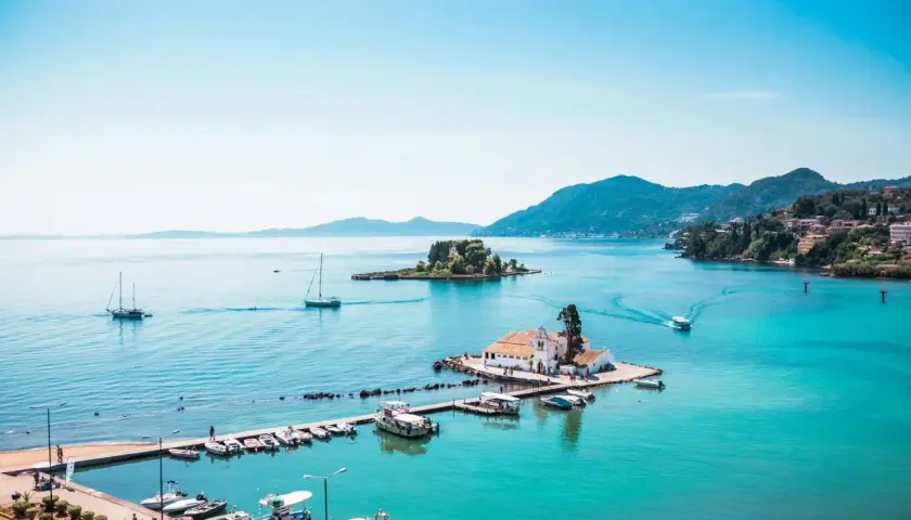 Vue idyllique de la baie de Corfou avec des bateaux, une église sur un îlot et des collines verdoyantes. Idéal pour savoir que faire à Corfou.