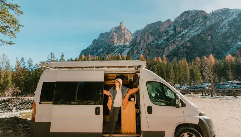 Une femme sort de son fourgon aménagé, profitant d'une vue spectaculaire sur les montagnes. Une image qui pourrait bientôt devenir un souvenir, car les fourgons aménagés vont être interdits.