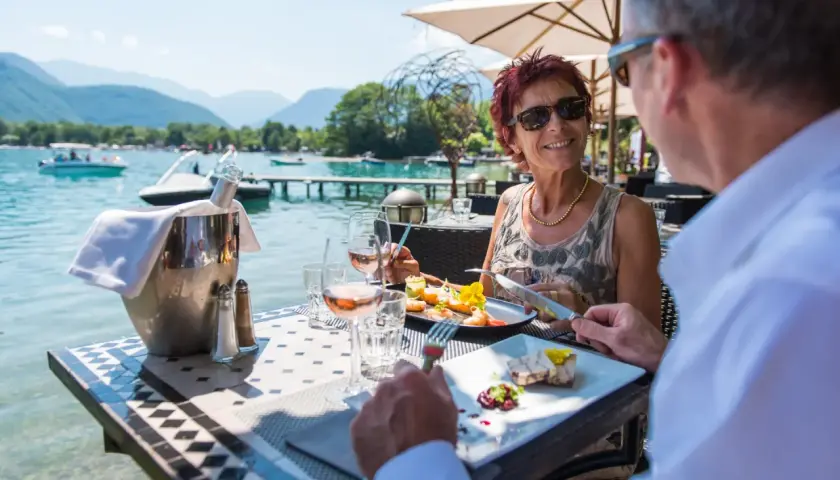 Un couple savoure un repas gastronomique avec vue sur le lac d'Annecy. La plage est magnifique.