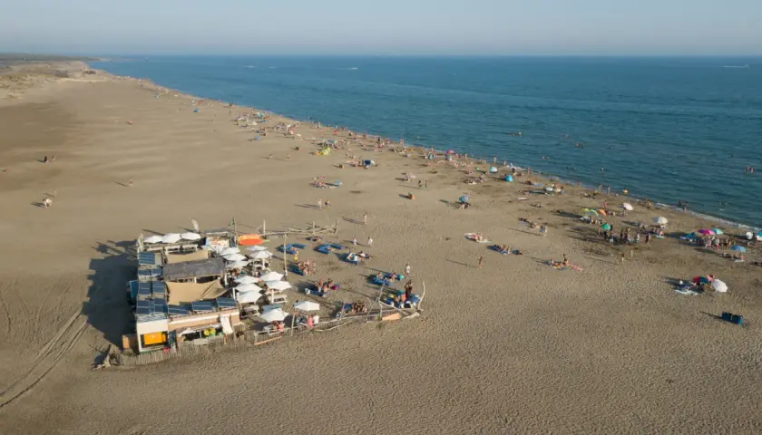 Vue aérienne d'une plage privée au Grau-du-Roi, avec des parasols, des transats et des baigneurs profitant du soleil et de la mer.