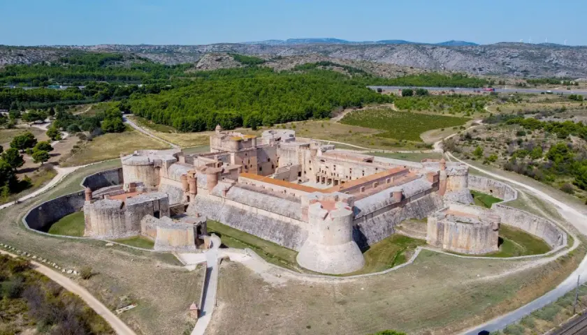 Vue aérienne du Fort de Salses, une imposante citadelle sur la côte vermeille, entourée de verdure et de collines.