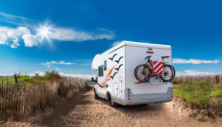 Camping-car prêt pour l'aventure sur une aire de camping car Ile de Ré, avec vélos à l'arrière, sous un ciel bleu éclatant.