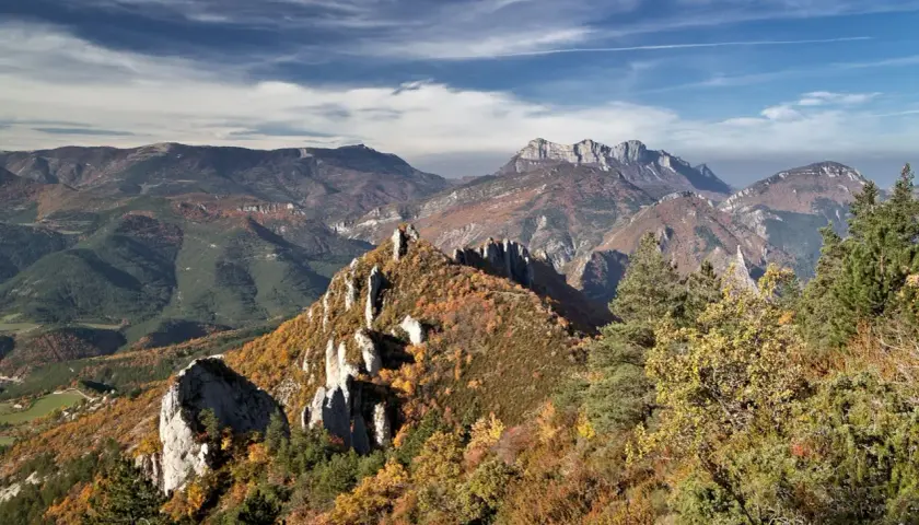 Vue panoramique des gorges de la Roanne en automne. Un sentier de randonnée serpente à travers des crêtes rocheuses et des forêts aux couleurs flamboyantes.