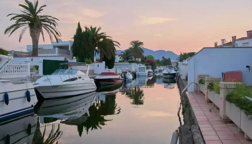 Coucher de soleil paisible sur les canaux d'Empuriabrava, Espagne, avec des bateaux amarrés et des palmiers se reflétant dans l'eau calme.