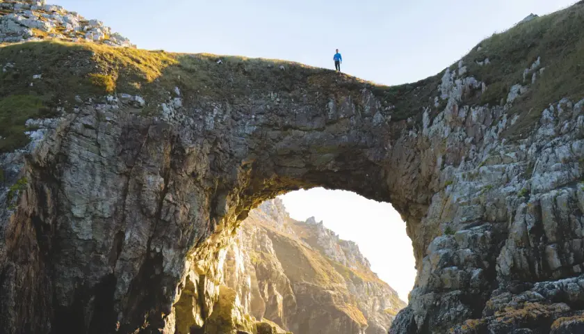 Un homme seul au sommet de la pointe de Dinan, surplombant un arc rocheux naturel.