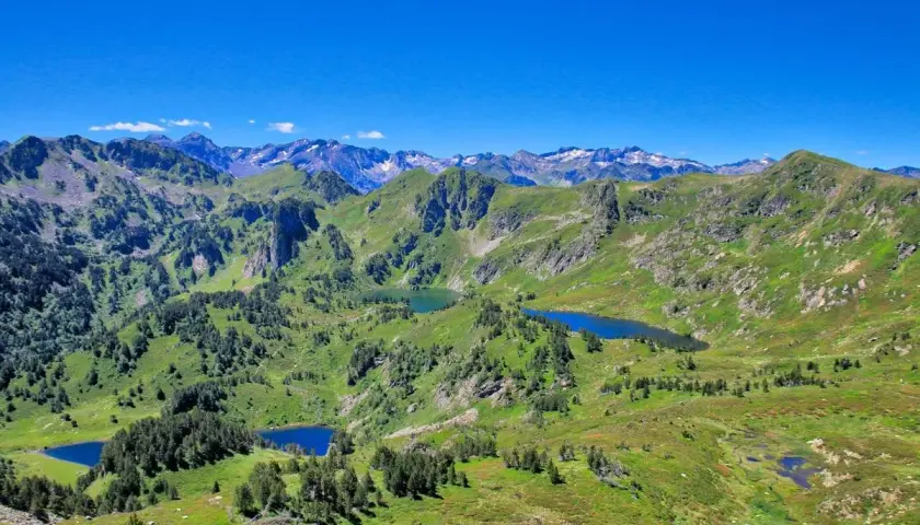 Vue panoramique sur les Pyrénées avec plusieurs étangs bleus, dont l'étang de Rabassoles, nichés dans des vallées verdoyantes sous un ciel bleu intense.