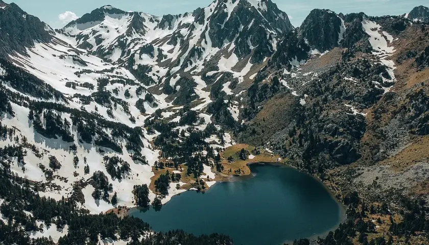 Vue aérienne du lac du Laurenti, niché au pied de montagnes enneigées et de forêts de pins. Un paysage alpin spectaculaire.