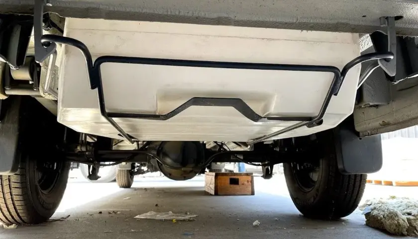 Vue sous un camping-car, montrant le réservoir d'eau propre fixé au châssis. Préparation pour le nettoyage de la cuve camping car.